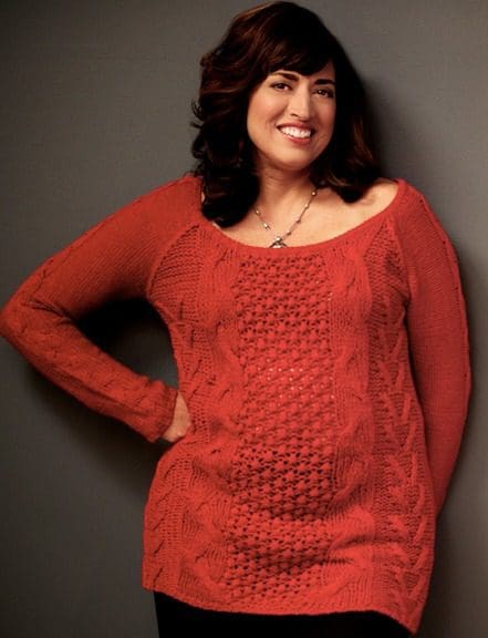 A woman in red sweater leaning on wall.