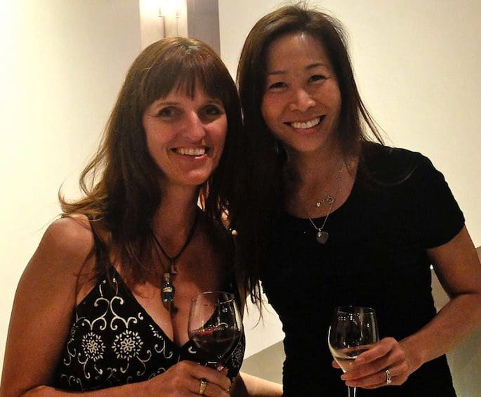 Two women posing for a picture with wine glasses.