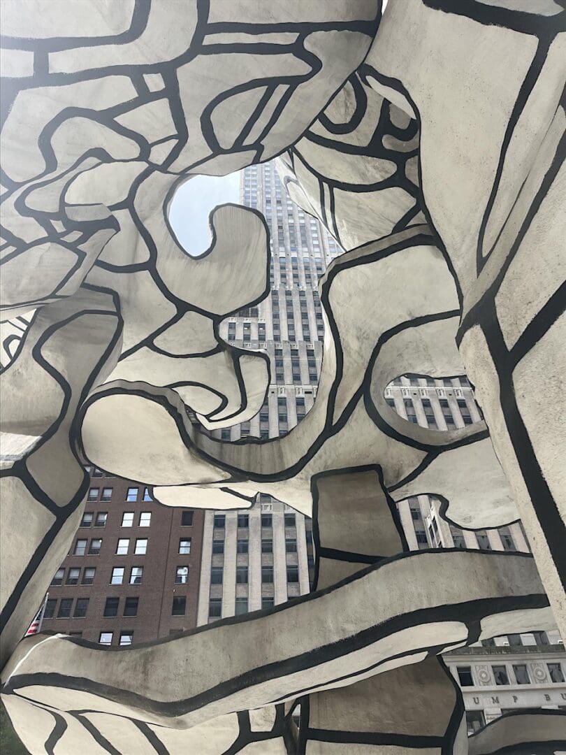 Abstract sculpture with buildings in the background.