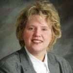 A woman with blonde hair wearing a gray suit.