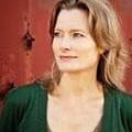 A woman in green shirt and necklace standing next to red wall.