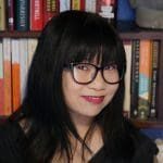 A woman with glasses and black hair in front of books.
