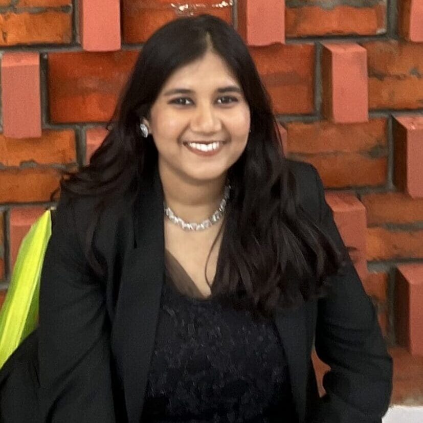 Smiling woman in formal attire against brick wall.