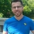 A man in blue shirt and glasses standing outside.